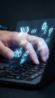 Hands typing on laptop keyboard with glowing digital icons and symbols floating above representing technology, connectivity and data processing.
