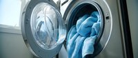 Modern washing machine with open door showing blue towels inside during laundry cycle in bright domestic interior for household cleaning concepts.