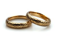 Hammered gold wedding bands with textured surface pattern on white background, matching pair of rings showing unique artisanal metalwork detail.