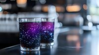 Magical galaxy-themed cocktails with purple and blue gradient colors showing constellation patterns, served in clear glasses on dark bar counter.