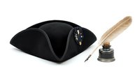 Tricorn hat in black velvet with decorative gold embellishments displayed alongside a quill pen and inkwell, isolated on white background for design and historical costume projects.