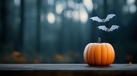 Orange pumpkin on wooden surface with flying paper bats against dark moody forest background, halloween seasonal decoration with bokeh effect.