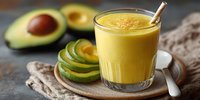 Fresh avocado smoothie in glass with sliced fruit on rustic wooden background, healthy breakfast or snack option for nutritious diet.