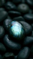 Glowing labradorite gemstone with blue and green iridescence resting among dark wet pebbles, showcasing natural mineral beauty.