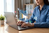 Young Asian businesswoman working on laptop with digital marketing icons floating above screen showing advertising and promotional concepts in modern office.