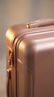 Rose gold hard shell suitcase with gold zipper details, close-up shot for travel, fashion, and luxury lifestyle content.
