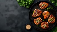 Grilled teriyaki chicken breasts with sesame seeds and green onions on black round grill pan, surrounded by fresh herbs on dark background.