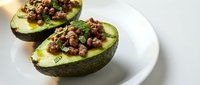 Avocado halves topped with seasoned ground beef, diced tomatoes, and fresh herbs served on white plate for healthy meal prep and nutritious lunch ideas.