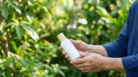 Senior man holding white spray bottle with green foliage background, suitable for gardening, pesticide, herbicide, skincare, sunscreen, or household cleaning product marketing.