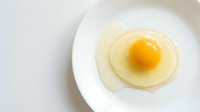 Fresh fried egg with bright yellow yolk on white plate against clean background for breakfast cooking and healthy nutrition concepts.
