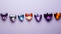 Colorful heart-shaped gemstones arranged in row on purple background. Crystal hearts in different colors including amethyst, diamond, topaz, and amber create romantic layout.
