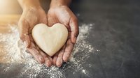 Hands holding heart-shaped dough with flour dust on dark surface. Baking, cooking, love concept for Valentine's Day, romantic recipes, homemade treats.