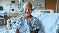 Young patient with bright smile resting in hospital bed during cancer treatment, wearing hospital gown, medical equipment visible in background, showing resilience and hope.
