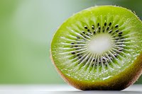 Fresh juicy kiwi fruit cut in half showing detailed seeds and flesh pattern in macro photography against soft green background, healthy food concept.