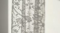 Delicate lace curtain casting intricate shadows on white wall, creating elegant pattern play of light and texture for interior design and home decor projects.