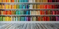 Colorful books arranged by spectrum colors on wooden shelves against wall with rustic wooden floor, creating rainbow library effect. For education and learning concepts.