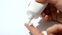 Male hand applying white cream, lotion, or skincare product from bottle dispenser on finger against white background for cosmetics, beauty, dermatology, and wellness use.