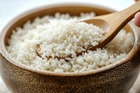 Steamed white rice in wooden bowl with bamboo spoon, close up view of fluffy cooked grains showing texture and individual kernels in natural lighting.