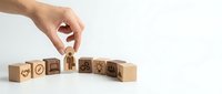 Hand placing wooden cube with house icon completing bridge of blocks with various symbols representing business growth and development concepts.