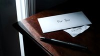 Handwritten envelope labeled For You with a sorry note and pen on a dark wooden table near a window, evoking emotion.