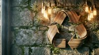 Wooden recycling symbol on rustic stone wall with glowing Edison bulbs and air plants, eco-friendly sustainability concept.