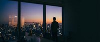 Silhouette of a man standing at large windows overlooking a sprawling cityscape during golden hour sunset, urban contemplation and success concept for business and lifestyle use.