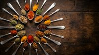 Colorful spices and herbs arranged in wooden spoons on rustic wood background. Cooking ingredients for culinary recipes and seasoning preparation.