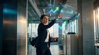 Professional Asian businessman in suit analyzing holographic financial data charts with upward growth trends in modern glass office environment.
