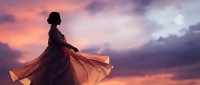 Young woman in flowing dress dancing at sunset with dramatic purple and pink sky creating silhouette against colorful twilight clouds for lifestyle content.