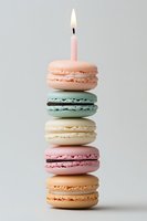 Stack of colorful macarons with lit birthday candle on top for celebration dessert and party treats on neutral background.