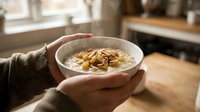 Person holding bowl of oatmeal porridge with nuts and seeds for breakfast, healthy eating and nutrition concept in kitchen setting.