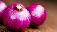 Fresh purple onions with vibrant layers on rustic wooden background, macro food photography highlighting natural texture and bright magenta color.