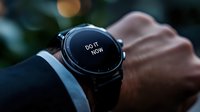 Modern smartwatch displaying motivational message "Do it now" on dark screen with blurred bokeh background, worn on male wrist in business attire setting.