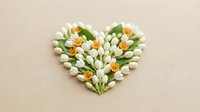Heart-shaped arrangement of white tulips and orange flowers on beige background for romantic greeting cards, wedding invitations, and spring decor.