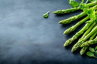 Fresh green asparagus spears arranged on dark slate background with copy space for culinary and healthy eating concepts.