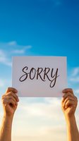 Hands holding white paper sign with sorry message against bright blue sky with clouds for apology and forgiveness concepts.
