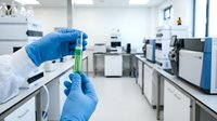 Scientist in blue gloves holding green liquid test tube in modern laboratory for chemical analysis and research experiments.