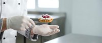 Professional chef hands presenting elegant berry tart dessert in modern kitchen. Culinary artistry showcase for restaurant menu and gourmet food presentation.