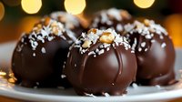 Dark chocolate truffles decorated with coconut flakes and nuts on white plate, selective focus with blurred golden bokeh lights in background. Sweet dessert.