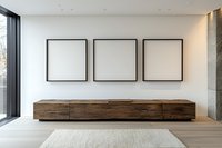 Modern minimalist interior with three empty black square frames on white wall above long wooden cabinet, panoramic window and light carpet flooring.