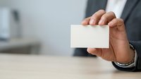 Businessman holding blank white business card in hand at office desk for corporate branding and professional networking purposes.