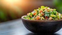 Fresh vegetable salad with chickpeas and herbs in rustic wooden bowl on dark table, selective focus with natural sunlight and blurred background.