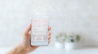 Female hand holding smartphone displaying shopping cart icon with sparkle effect overlay, representing digital commerce and mobile shopping experience.