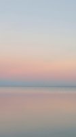 Serene dawn seascape with soft pastel gradient sky transitioning from blue to pink and peach tones over calm ocean waters, ideal for wellness and lifestyle backgrounds.