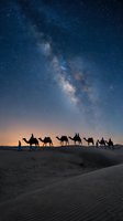 Camel caravan silhouettes crossing desert dunes under spectacular Milky Way galaxy with countless stars in deep blue night sky for travel and adventure concepts.