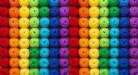 Colorful rainbow gradient pattern of round plastic buttons arranged in rows. Bright vibrant spectrum from red to purple for crafting and sewing projects.