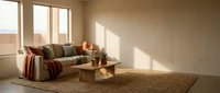 Modern minimalist living room with beige sofa, wooden coffee table and warm natural sunlight streaming through large windows creating cozy atmosphere.