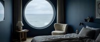 Modern bedroom with round porthole window overlooking ocean, featuring navy walls, contemporary furnishings, and coastal nautical design for interior decoration and home styling projects.
