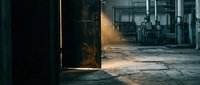 Abandoned industrial warehouse interior with weathered metal door, dusty floor, and machinery visible through doorway, suitable for urban decay and industrial design projects.