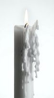 Burning white pillar candle with melting wax drips and glowing flame, isolated on a light background for decoration and ambiance concepts.